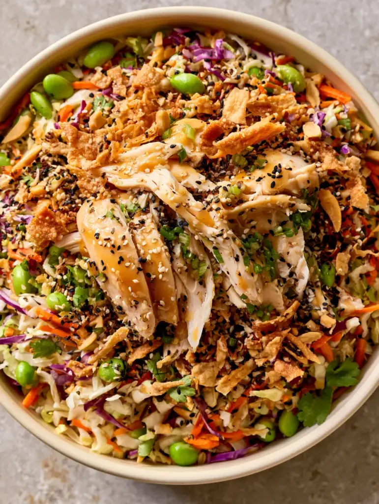 Top-down view of the Asian crunch chicken salad showing glossy dressing and heavy sesame seed garnish.