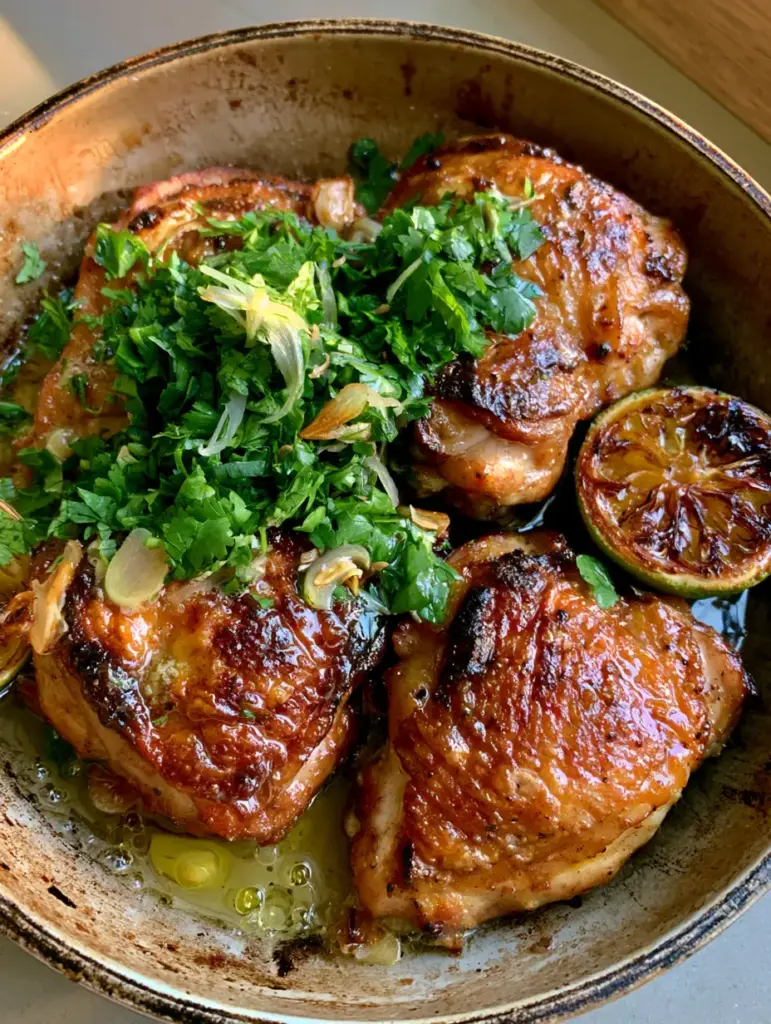 Cilantro Lime Chicken with Crispy Skin and Zesty Garlic Butter Glaze 1 Top-down shot of charred lime wheels and pan-seared chicken in a rustic cast iron skillet on a wooden table.