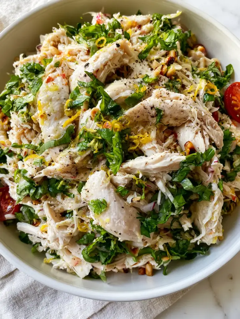 Lemon Basil Chicken Salad with Toasted Pine Nuts and Zesty Lemon-Olive Oil Dressing 1 A white ceramic bowl filled with Lemon Basil Chicken Salad on a marble countertop with a linen napkin.