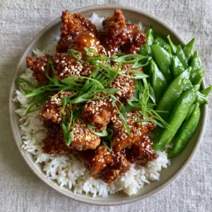 Close up of crispy air-fried chicken chunks coated in amber honey-garlic glaze for a Sesame chicken recipe.