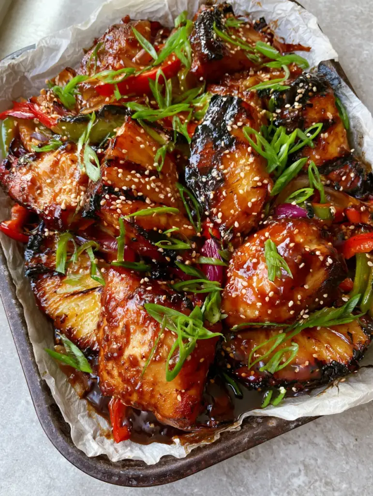 Gluten-free Hawaiian Chicken with Caramelized Pineapple and Glossy Teriyaki Glaze 2 Close up handheld photo of succulent seared chicken chunks drenched in glossy amber teriyaki glaze on wrinkled white parchment. (Gluten-free Hawaiian Chicken)